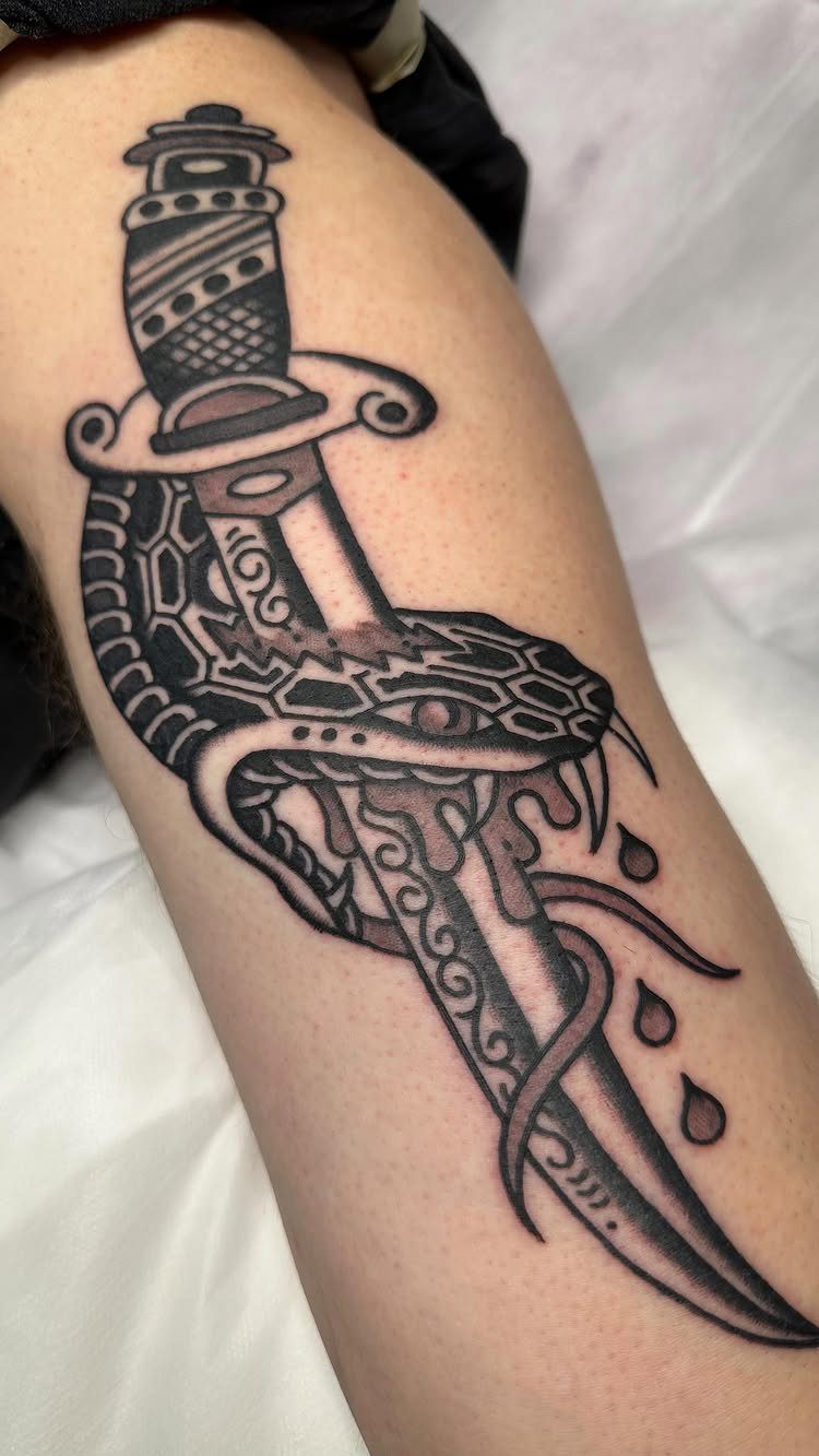 Traditional black ink tattoo of a dagger and snake on a person's leg