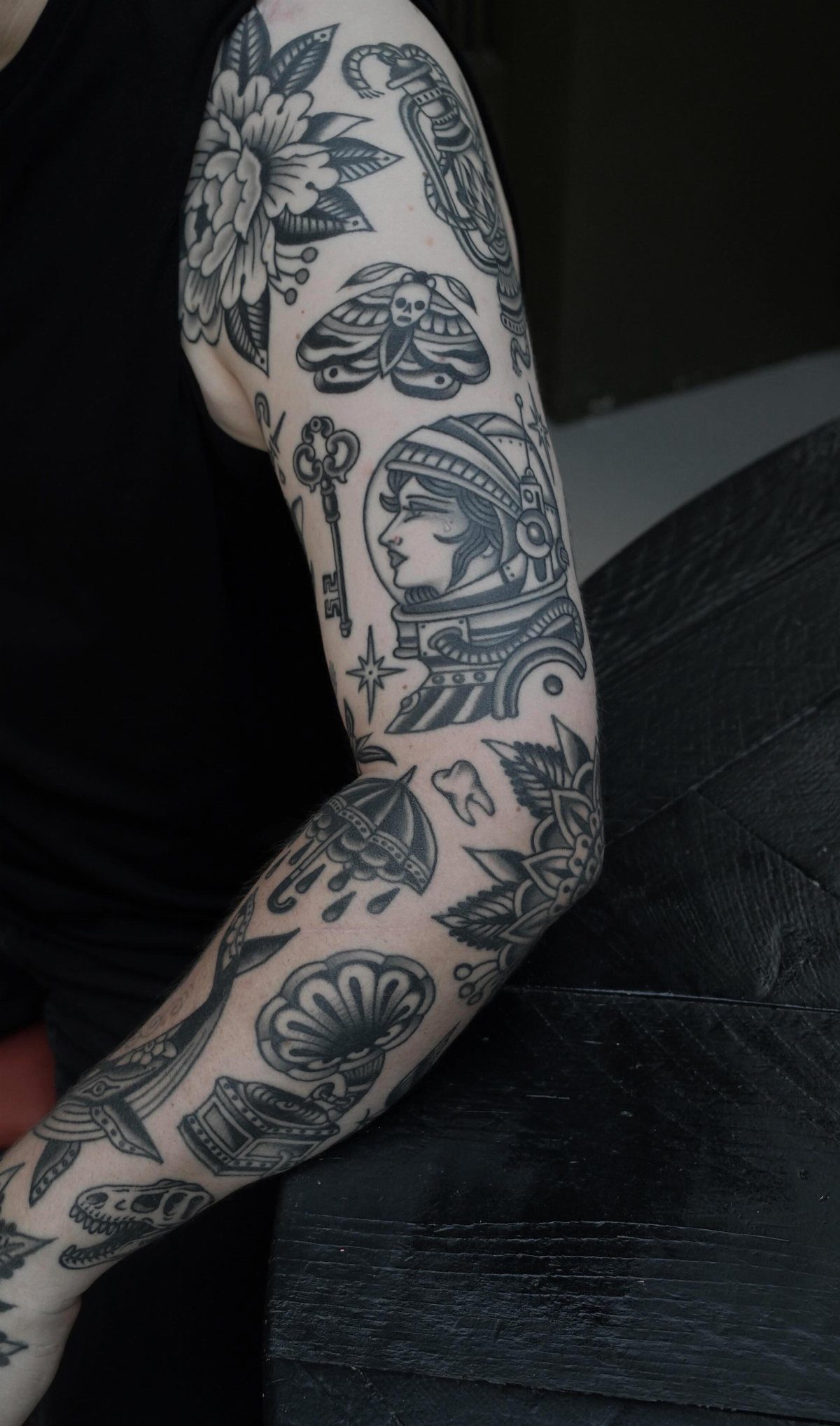 Tattooed arm featuring black and white traditional designs including an astronaut and flowers.