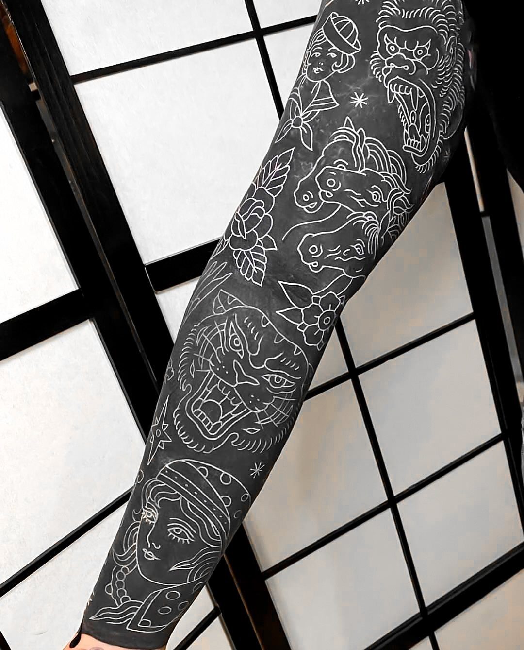 Tattooed arm with white line art on black ink against a shoji screen