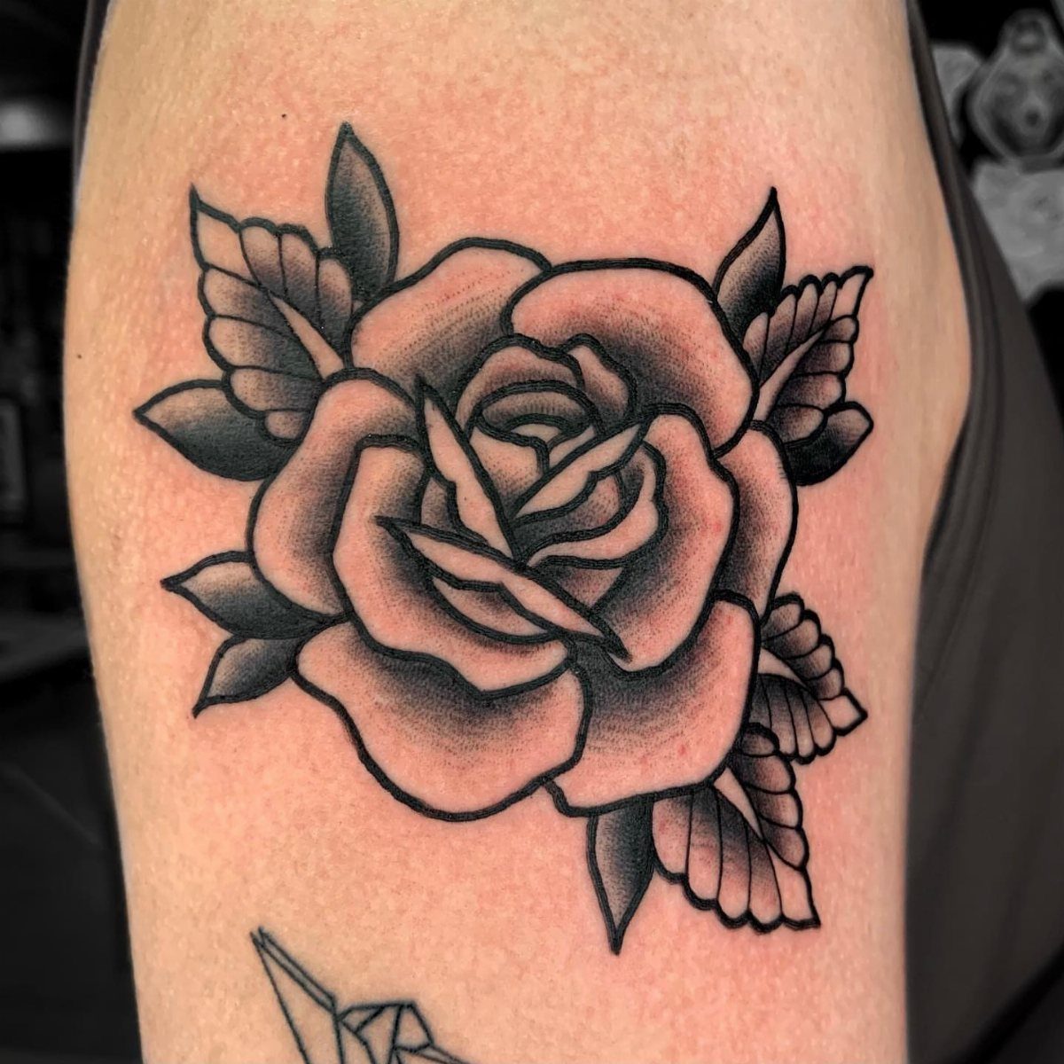 Traditional black and grey rose tattoo with bold outlines on human skin.