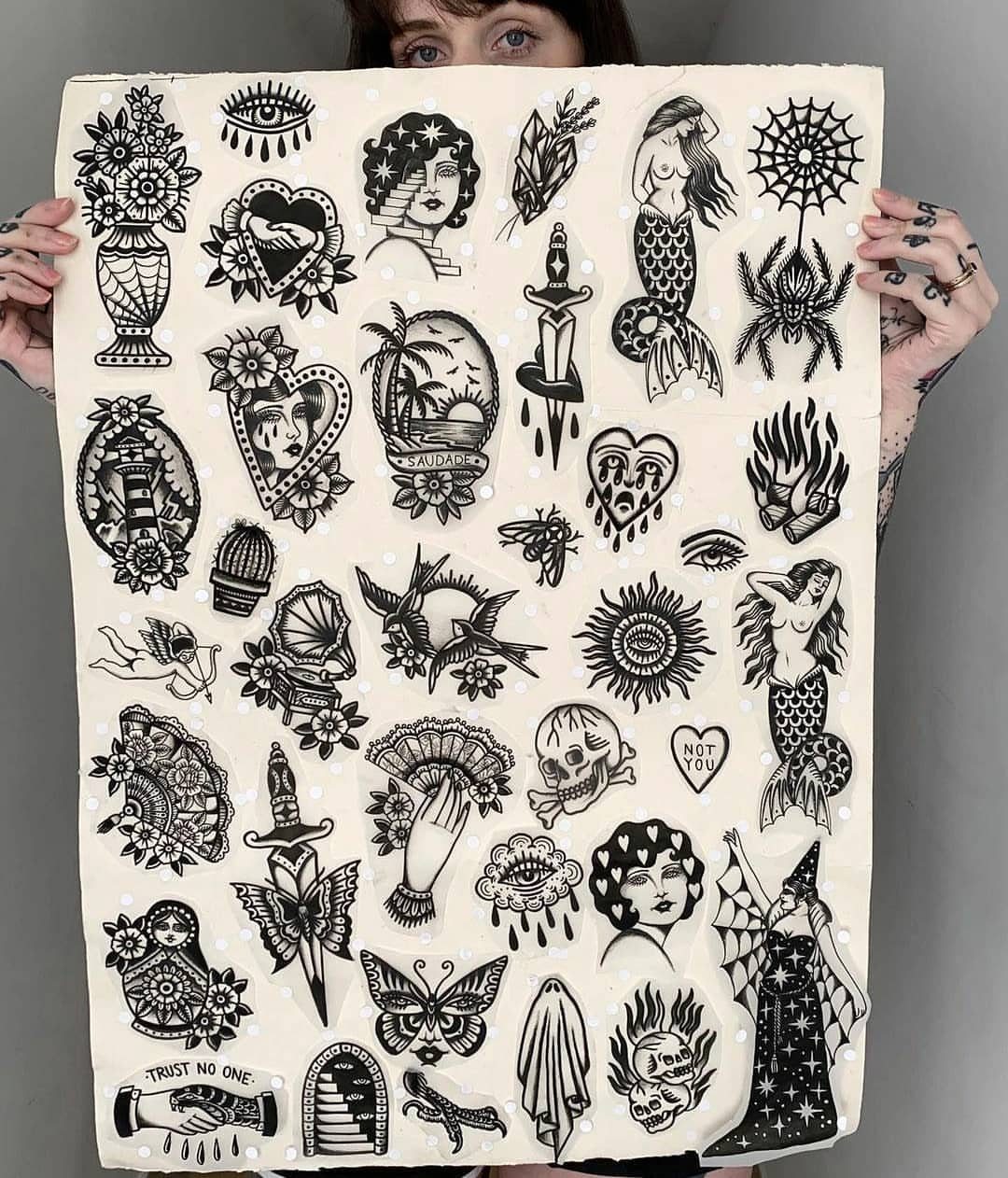 Tattoo flash sheet with various black ink traditional designs held by a person.