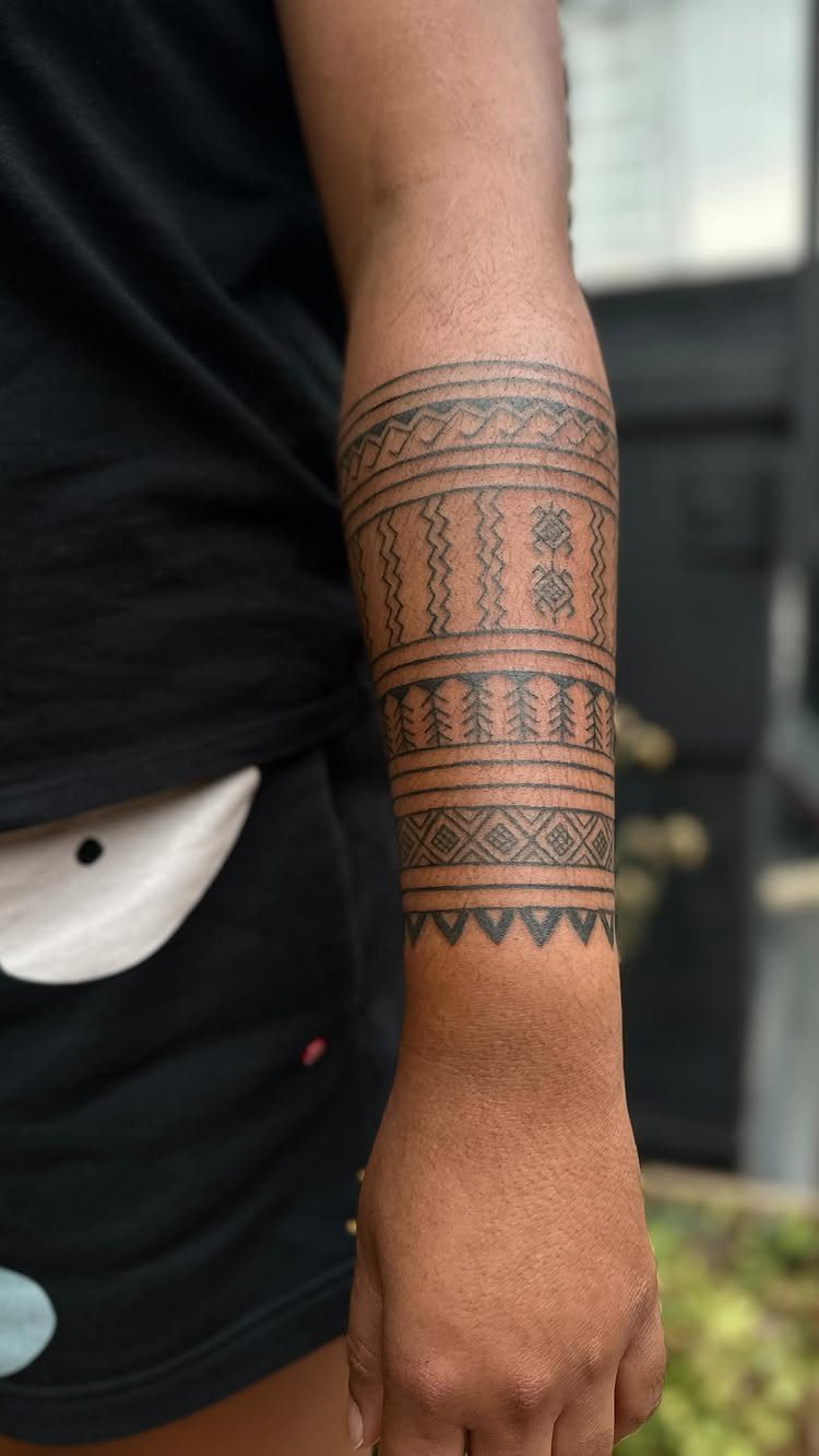 Forearm with a black ink geometric tribal tattoo band wrapping around the skin.
