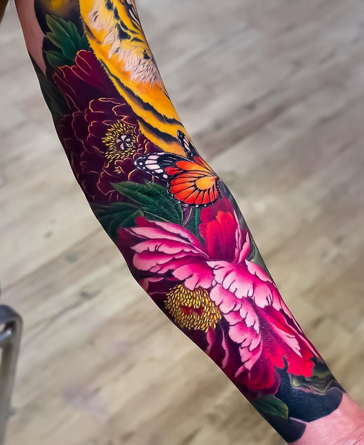 Colorful tattoo on an arm featuring a tiger, peonies, and a butterfly.