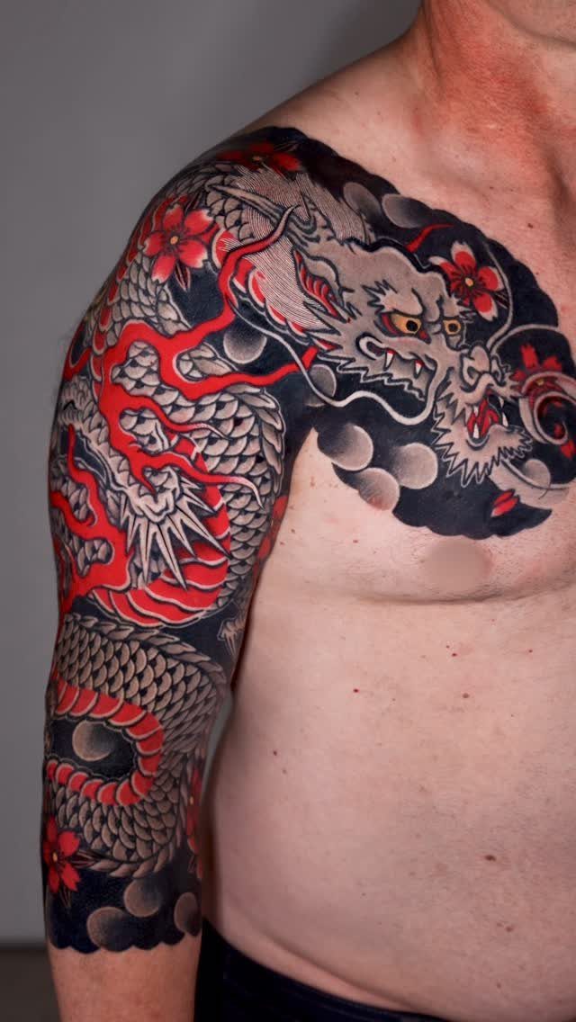 Dragon tattoo with red and grey ink covering a man's shoulder and arm.