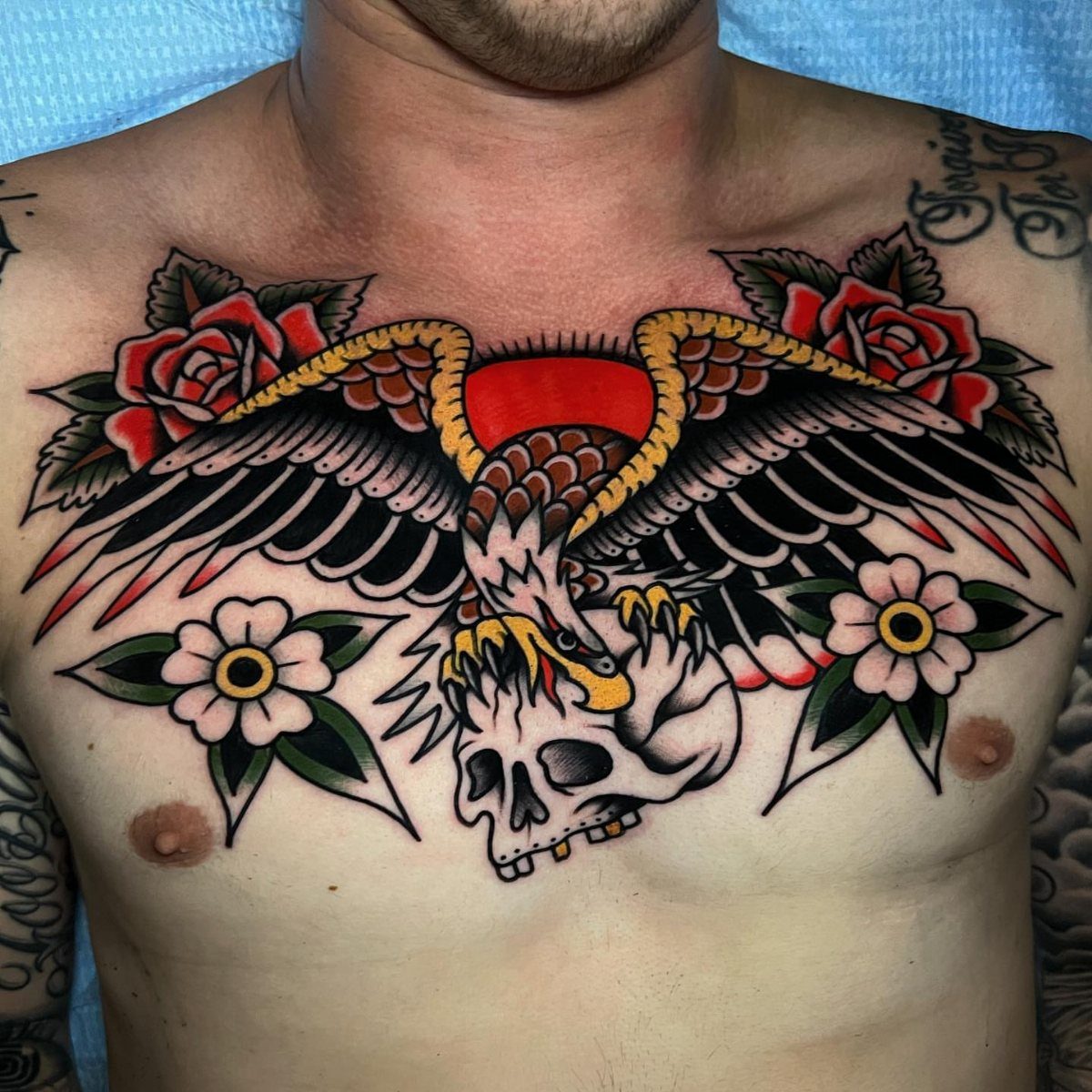 Eagle tattoo on a man's chest clutching a skull with red roses