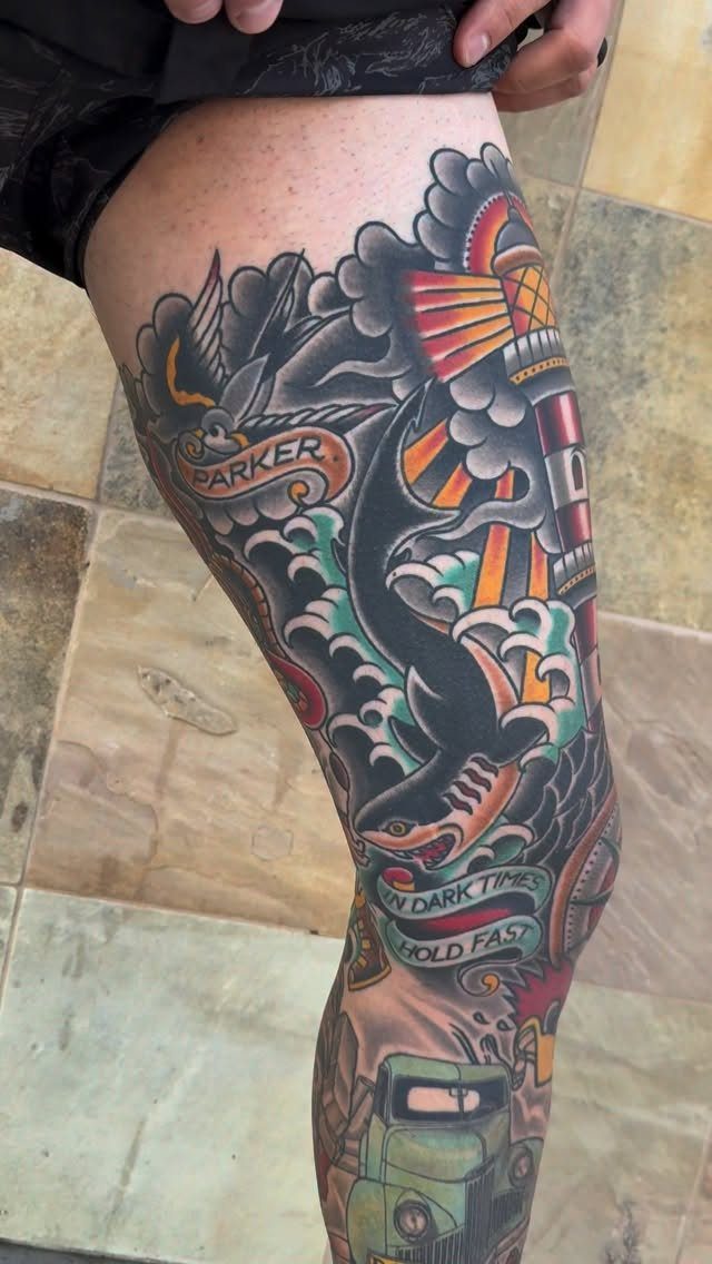 Traditional tattoo sleeve on a leg featuring a lighthouse, shark, and vintage car.