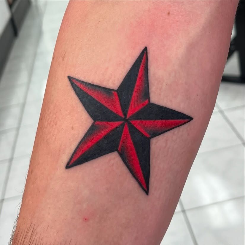 Five-pointed star tattoo with red and black shading on a person's arm.