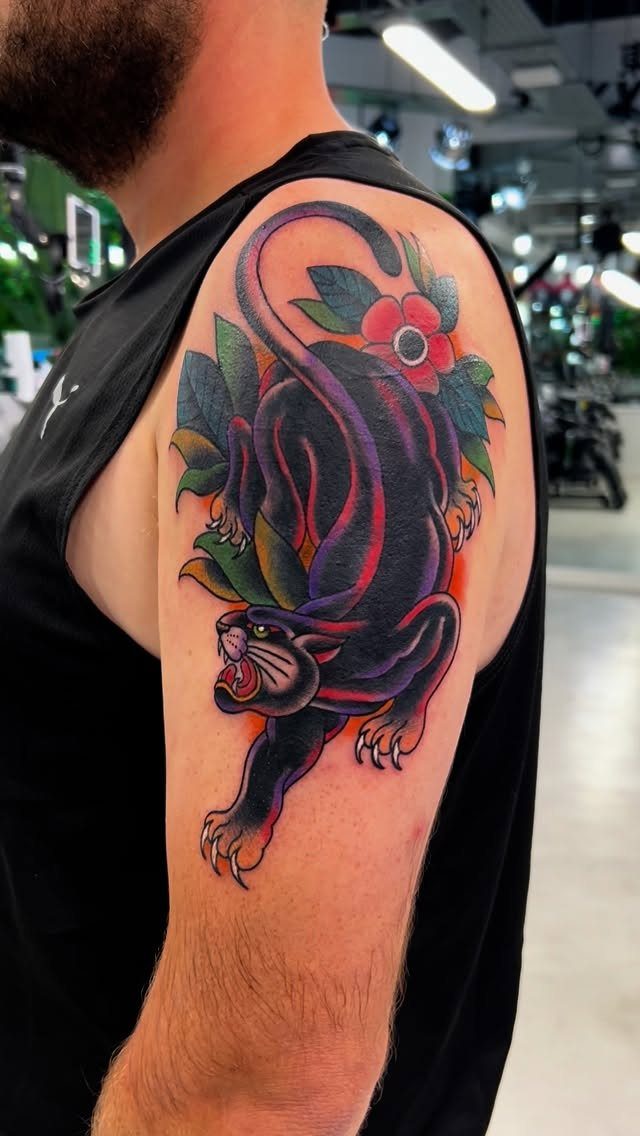 Black panther tattoo with red accents and flowers on a man's upper arm.