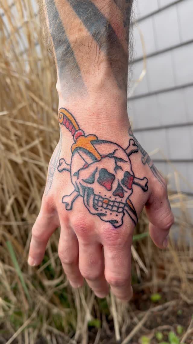 Traditional skull tattoo with crossbones and a dagger on a man's hand.