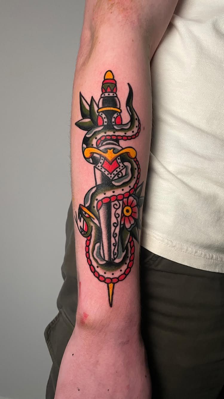 Traditional tattoo of a green snake coiled around a dagger on a man's forearm