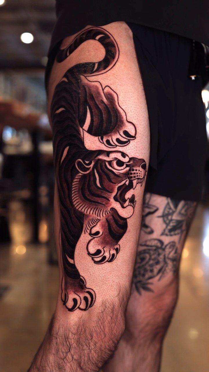Traditional tiger tattoo with bold lines and red accents on a man's thigh