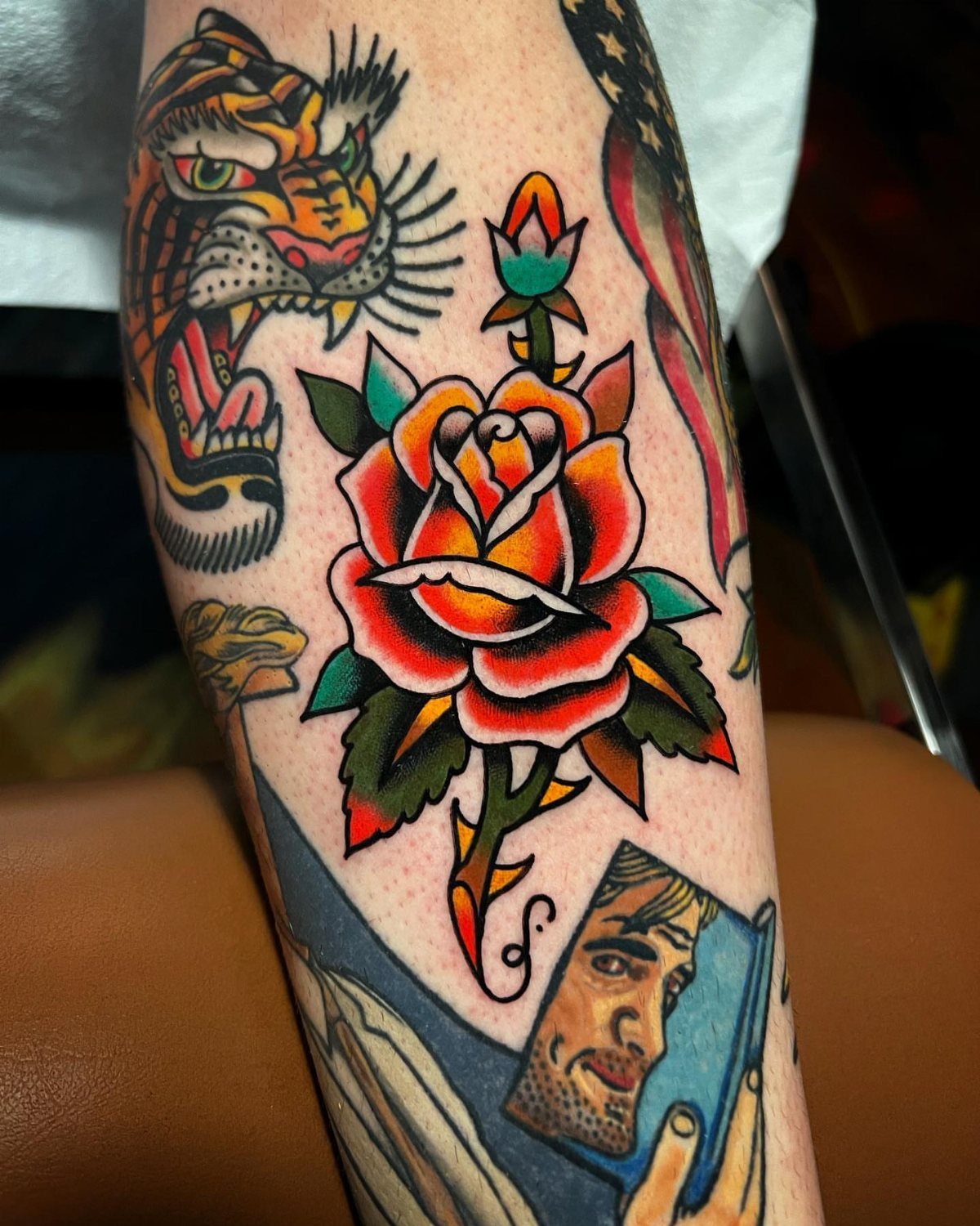 Traditional red rose tattoo with green leaves on a man's tattooed arm.