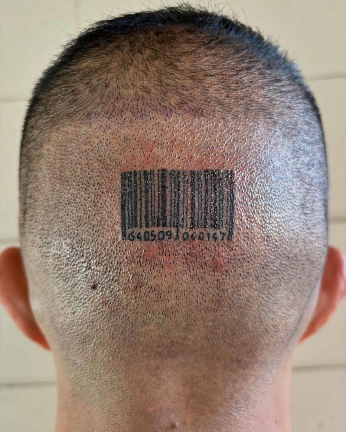 Barcode tattoo with numbers on the back of a person's shaved head