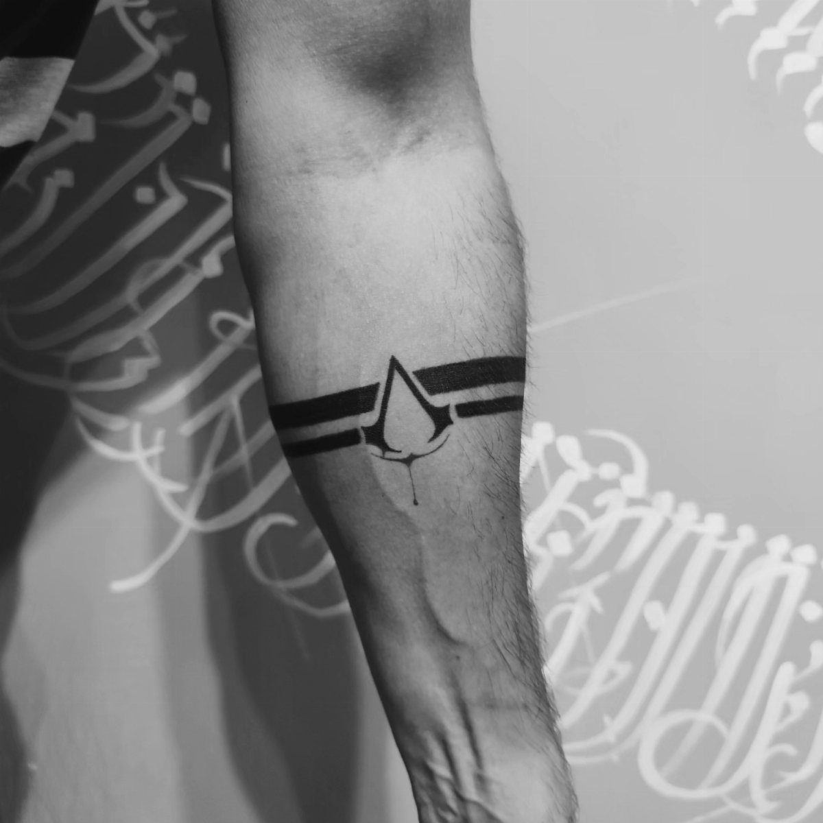 Forearm with a black ink Assassin's Creed logo tattoo wrapped in horizontal bands.