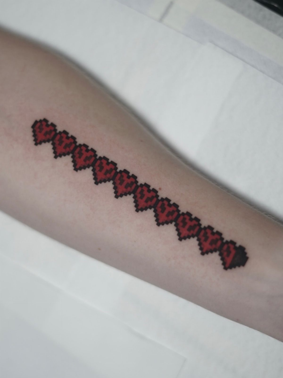 Pixelated red heart health bar tattoo on a person's forearm