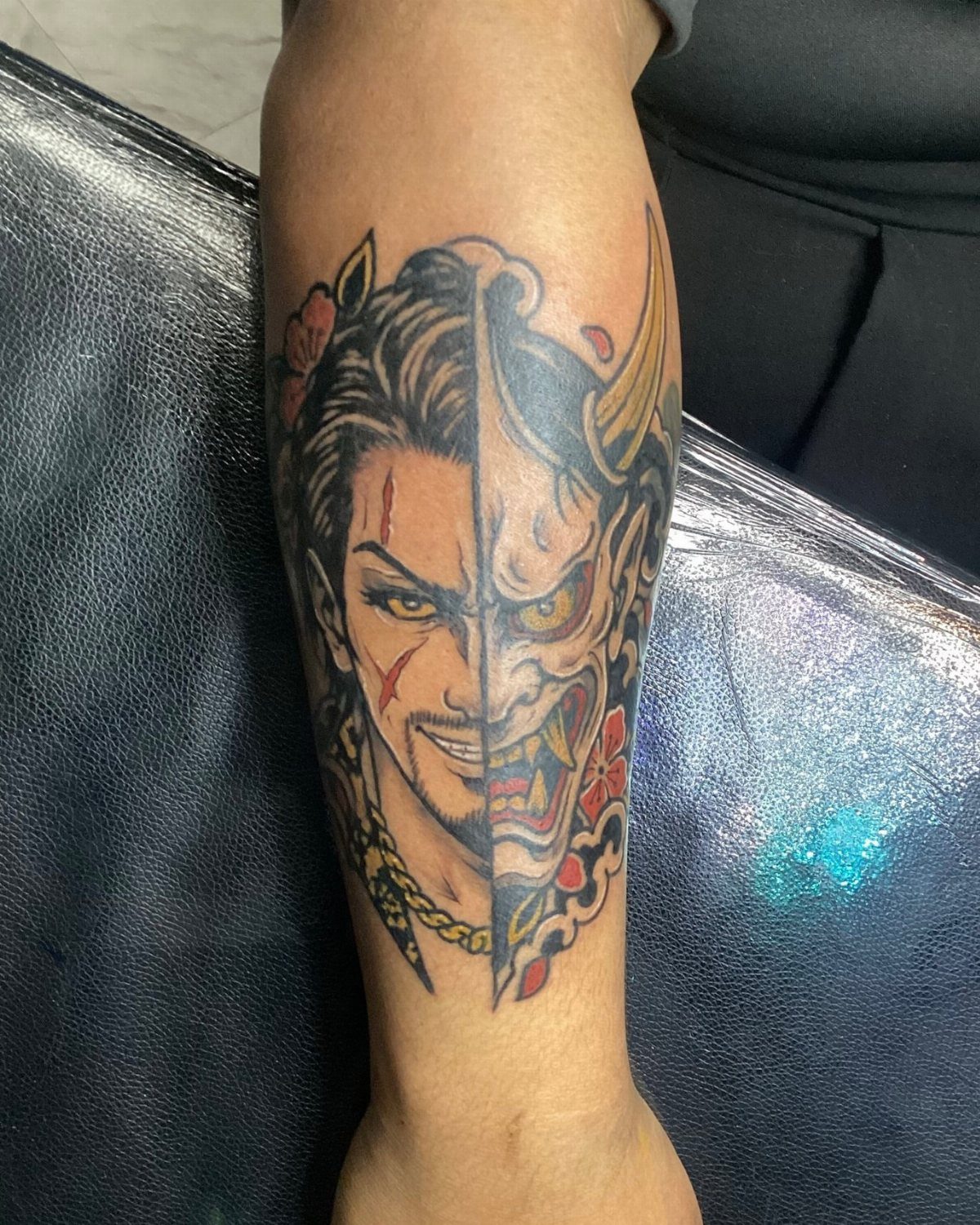 Forearm tattoo of a split face combining a man and a Japanese demon mask.