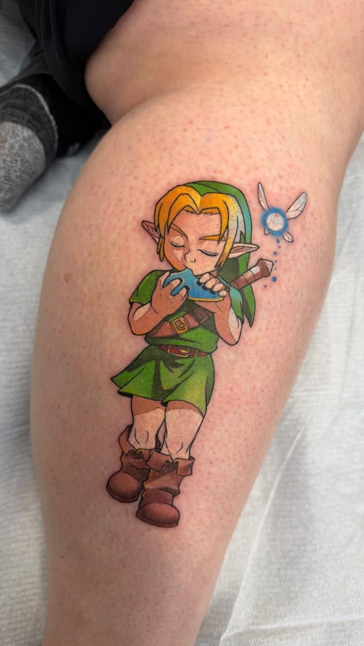 Link tattoo on a leg playing an ocarina with a small blue fairy