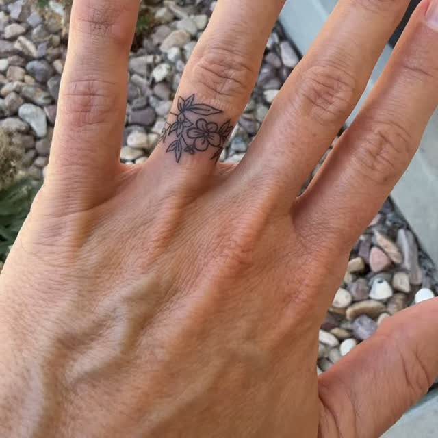 Floral ring tattoo on a person's finger against a background of small pebbles.