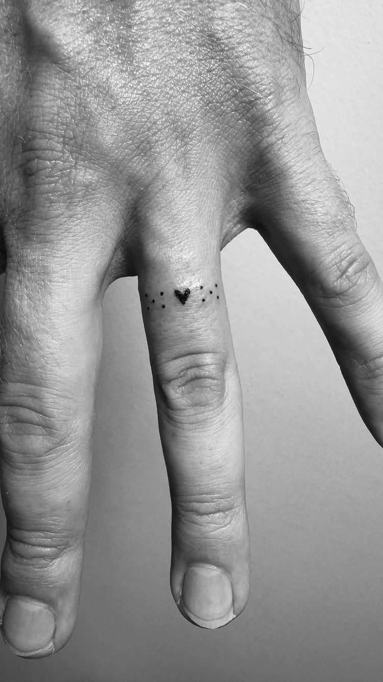 Small heart tattoo on a ring finger surrounded by a band of dots.