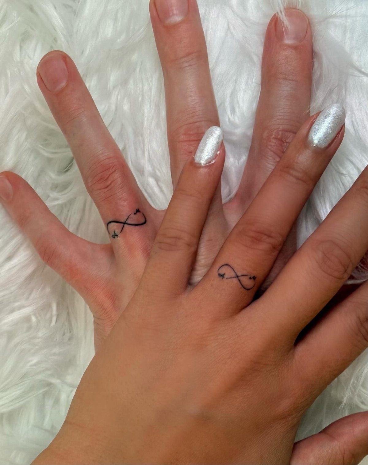 Two ring fingers with matching black infinity symbol tattoos on white fur.