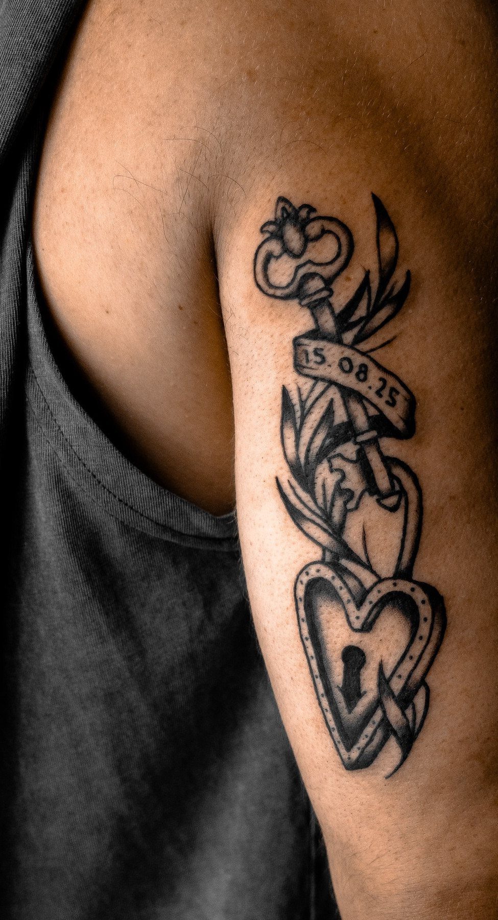 Lock and key tattoo with a date banner on a person's upper arm.
