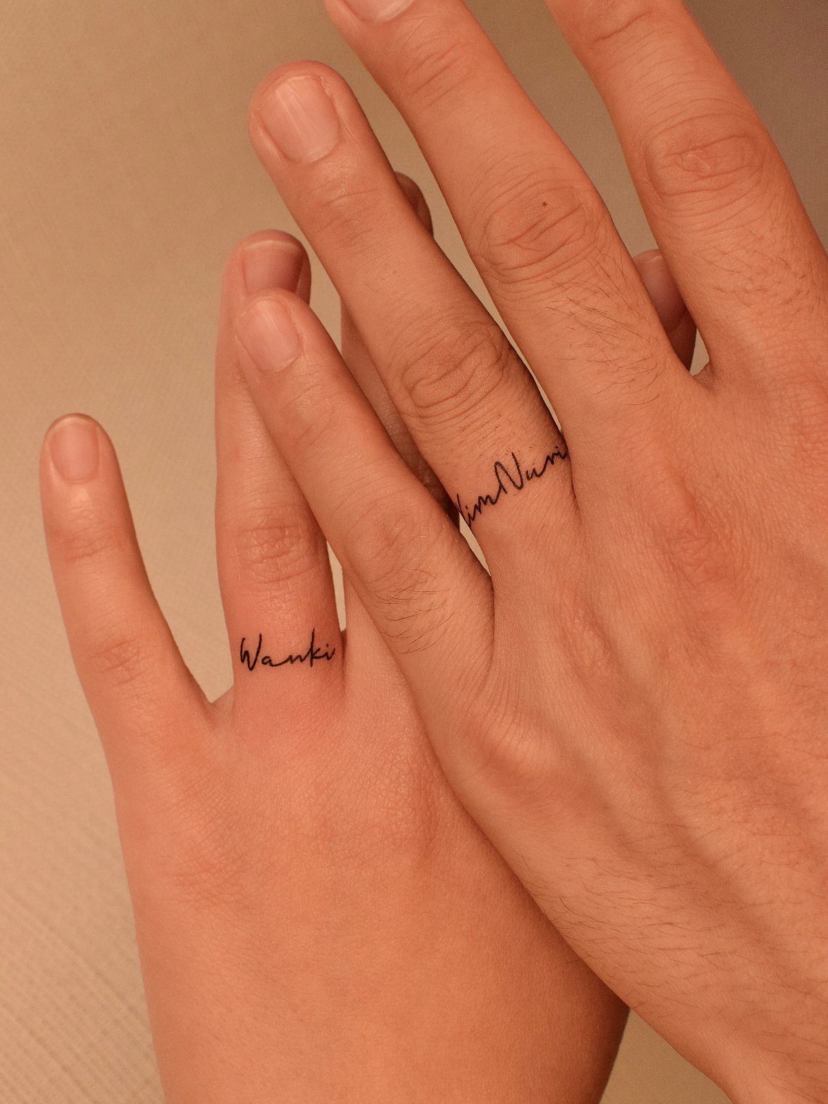 Two ring fingers with cursive script tattoos wrapped around them like wedding bands.