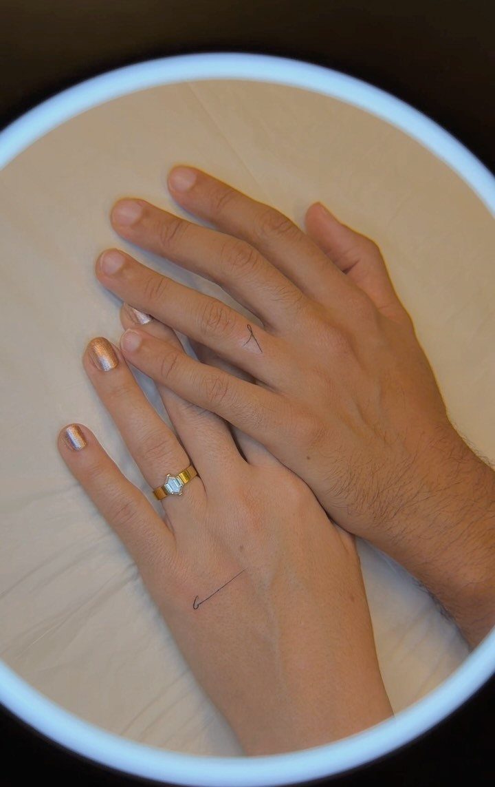 Two hands with matching thin black line ring tattoos on their ring fingers.