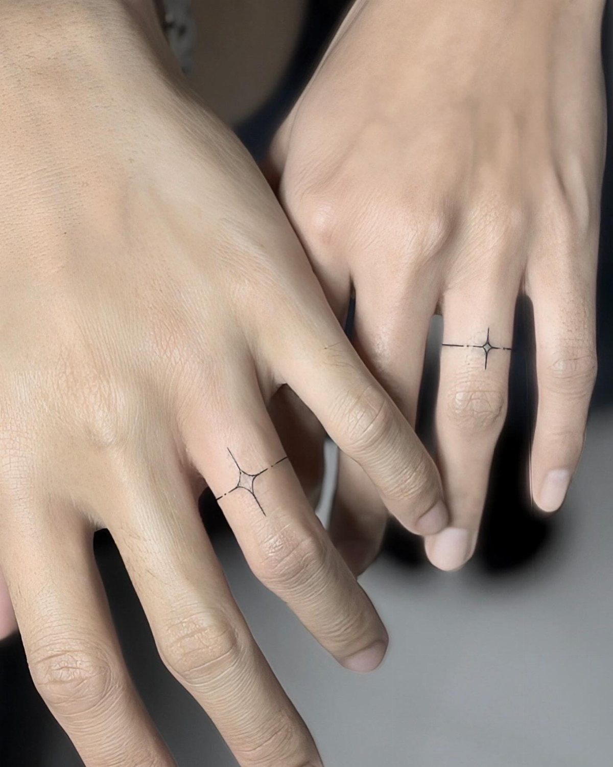 Two ring fingers with matching thin black line tattoos and small star accents.