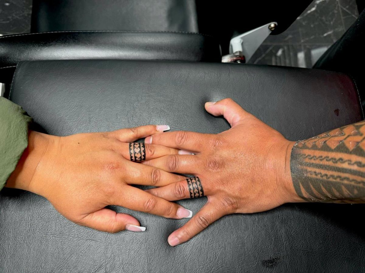 Two hands with matching geometric tribal wedding ring tattoos on their ring fingers.