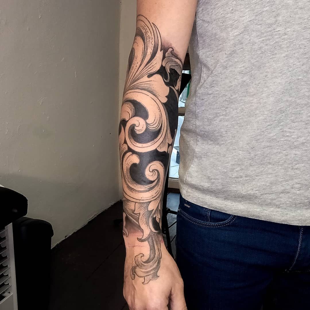 Acanthus leaf tattoo with flowing organic scrolls on a person's forearm.