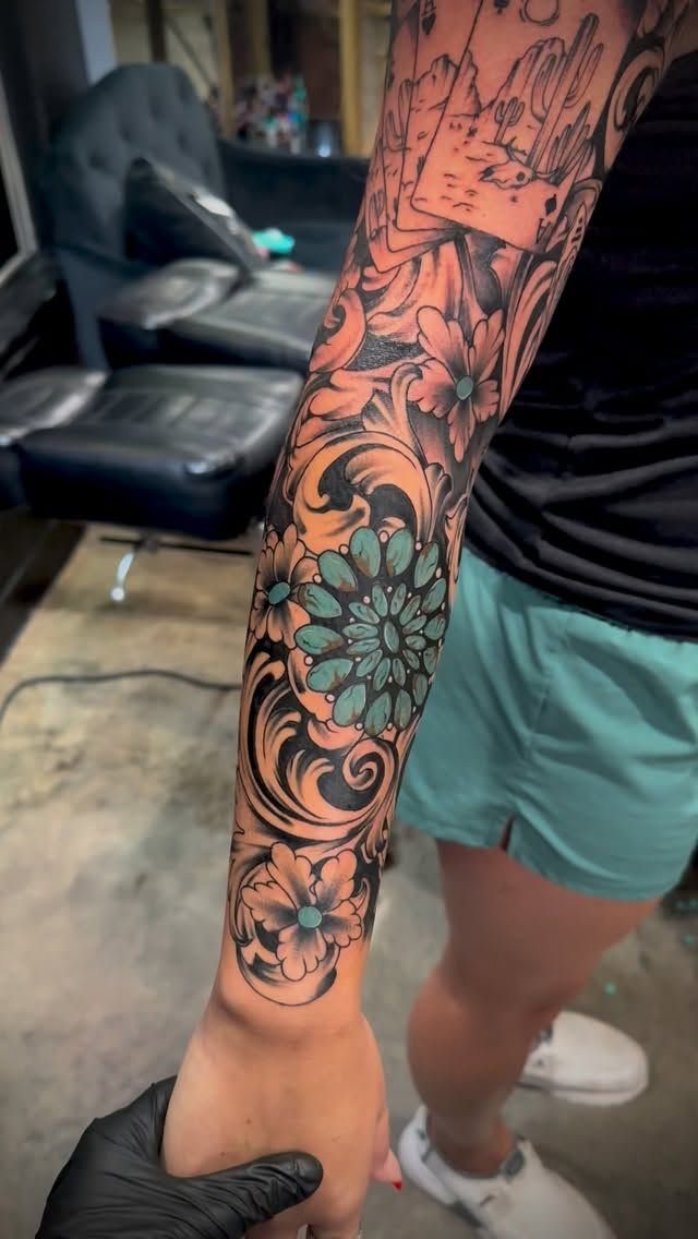 Forearm tattoo with carved leather tooling patterns, floral scrolls, and turquoise accents.