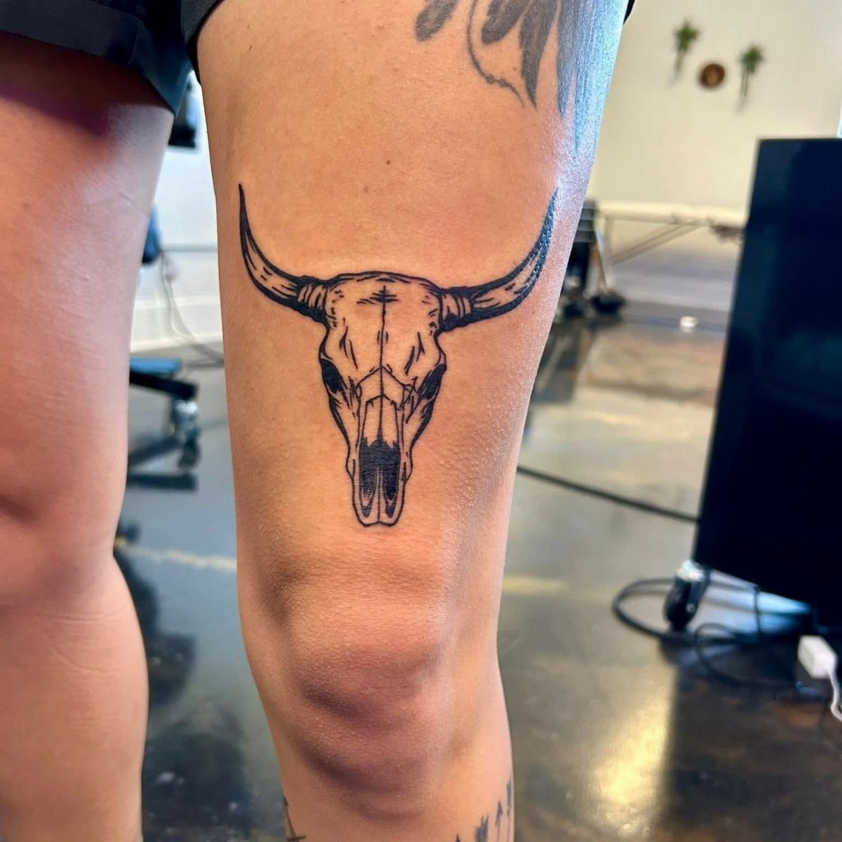Steer skull tattoo with long horns on a person's leg above the knee.