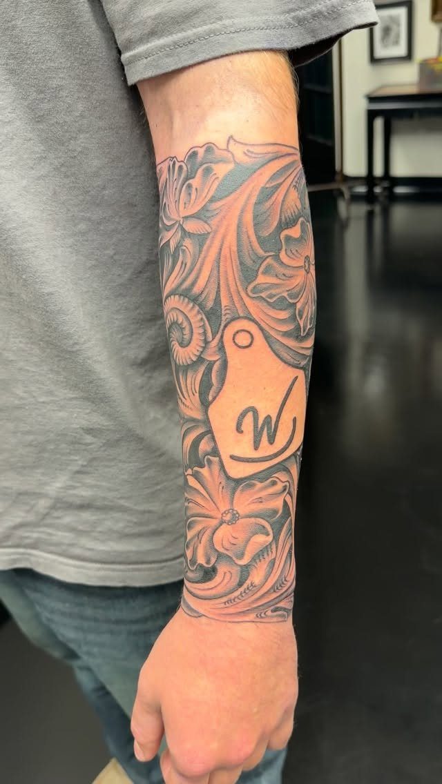 Forearm tattoo with black and grey western leather tooling floral scroll patterns.