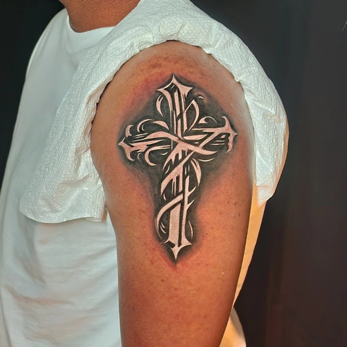 Ornate white ink cross tattoo with heavy black shading on a person's upper arm