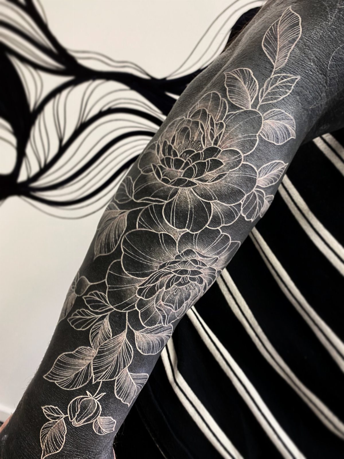 White floral tattoo with detailed petals and leaves over solid black ink on arm