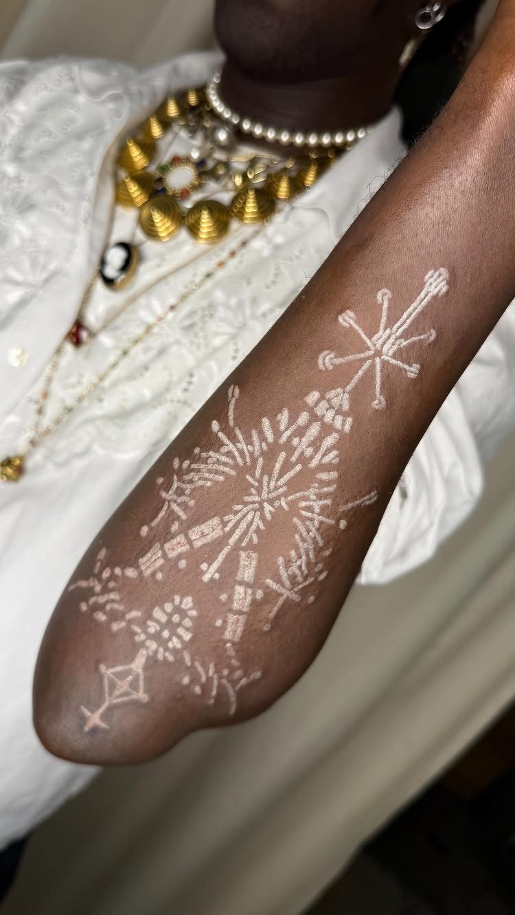 White ink tattoo with geometric patterns on a person's dark skin forearm.