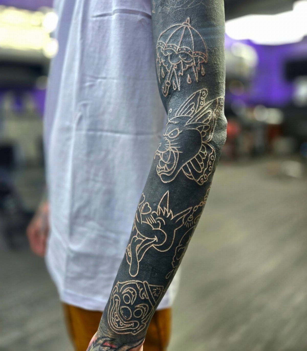 Arm with a black ink sleeve tattoo featuring white ink line art designs.