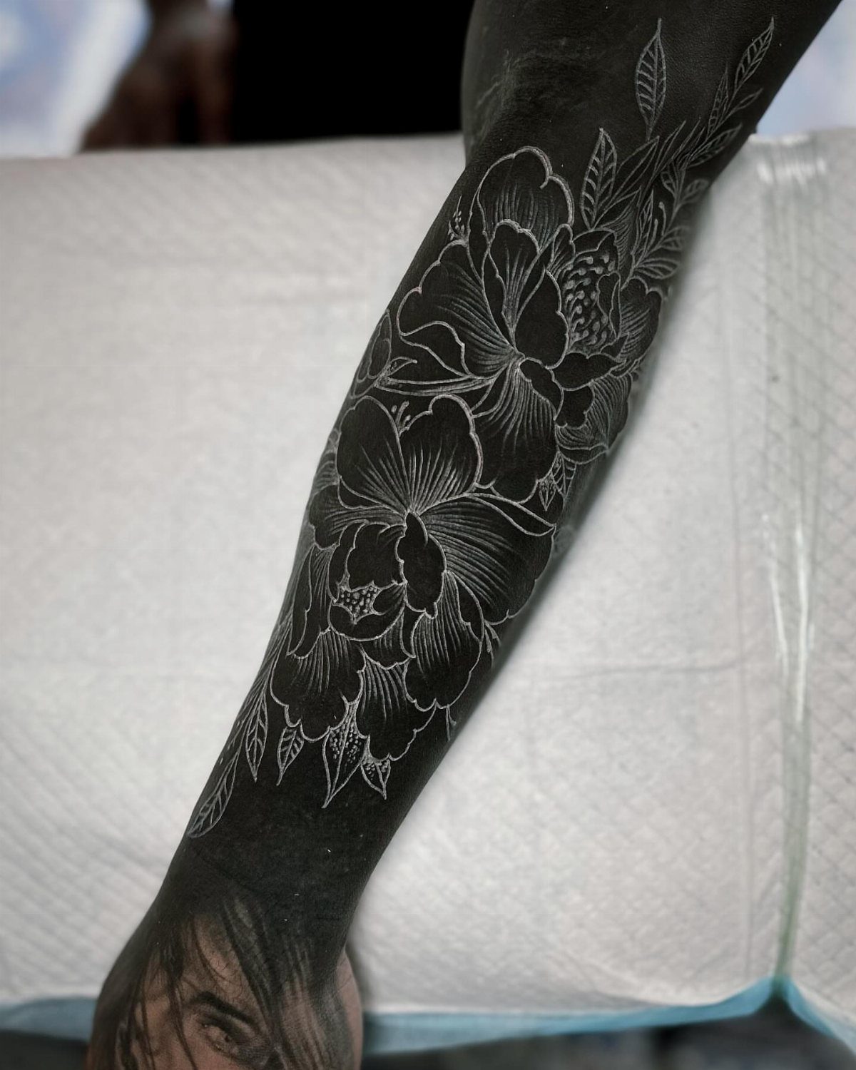White ink floral peony tattoo on a solid black ink arm sleeve