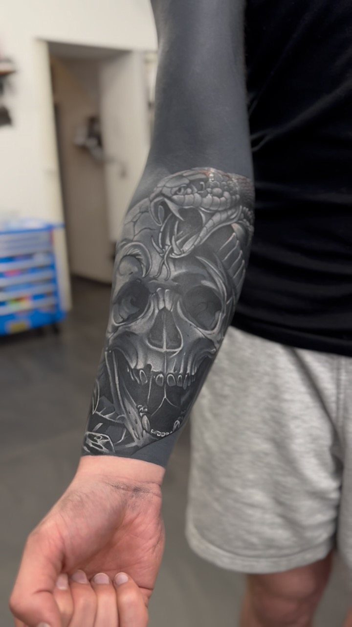 Skull tattoo on a forearm using white ink highlights over a black background.