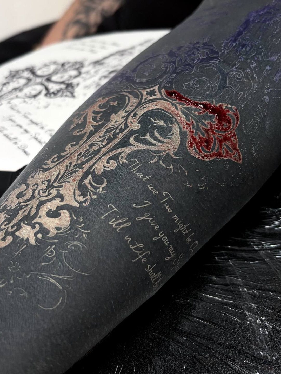 White ornamental tattoo and cursive text on blacked-out skin of a person's arm
